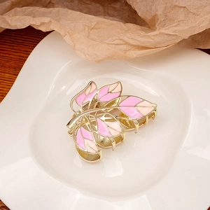 Detailed macro view of a golden leaf-shaped hair claw clip with pink enamel petals