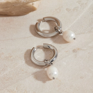 Silver stainless steel hoop earrings with white pearl pendants on beige stone surface