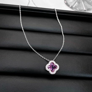 Detail of silver clover pendant necklace with purple gemstone on a black jewelry box