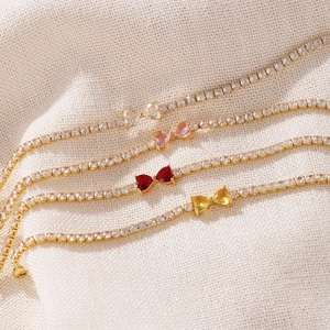 Detailed view of four colorful heart-shaped zircon tennis bracelets on white fabric.