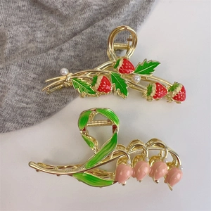 Detailed view of metal hair claws with enamel strawberry and lily designs and pearls