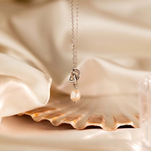 Detailed view of silver knot necklace with pearl on cream silk and shell background