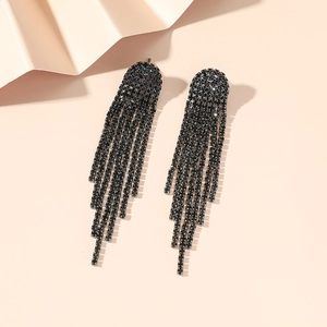 Flat lay macro of long black rhinestone tassel earrings on a soft pink surface