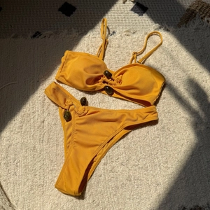 Detail of ribbed mustard yellow bikini featuring decorative resin buckles and textured fabric