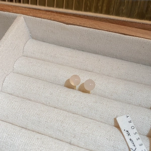 Close-up of pearl stud earrings with golden needles on a beige velvet jewelry box tray
