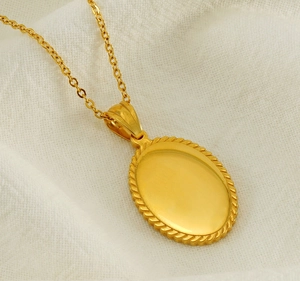 Macro detail of gold oval pendant with textured rope edge on white linen fabric