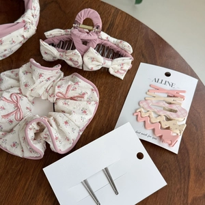 Floral scrunchie, bow claw clip, and pink hairpin set on a vintage wooden table