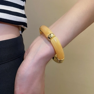 Détail d'un bracelet articulé en résine jaune et maillons dorés porté sur le poignet
