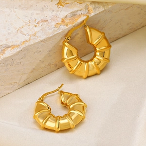 Fashionable 18K gold plated hollow bamboo hoop earrings on a textured stone background