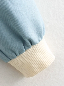 Detailed close-up of blue bomber jacket cuff with beige ribbed elastic knit stitching