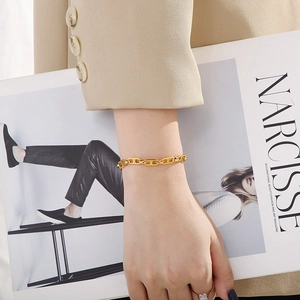 Close-up of a gold-toned stainless steel link bracelet worn with a stylish blazer