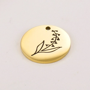Macro view of gold stainless steel round pendant featuring a black engraved floral pattern