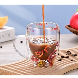 Pouring coffee into a double walled glass mug with dried flowers and wooden tray