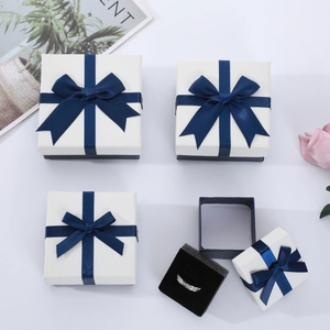 White jewelry gift boxes with navy blue ribbon bows and black velvet foam inserts