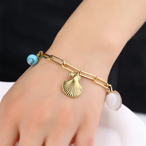 Detail of gold seashell bracelet with natural blue stone on a woman's wrist