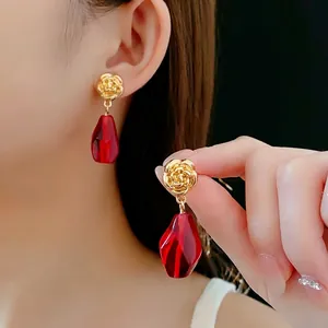 Elegant gold rose stud earrings with large red faceted glass drops worn by model