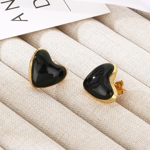 Close-up of black heart enamel earrings with gold metal frame on soft fabric