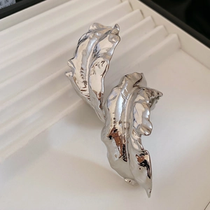 Macro shot of silver irregular leaf-shaped earrings with polished liquid metal texture