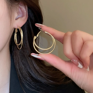 Close-up of golden double-hoop earrings featuring one smooth and one textured inner ring