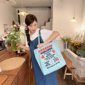 Close-up of light blue canvas tote bag with retro typography in a cozy cafe setting