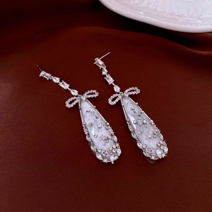 Detail of silver bow earrings with zircon studs and teardrop resin pendants on velvet