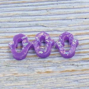 Macro detail of three purple resin Hamsa hands with colorful opal glitter on wood
