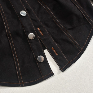 Dettaglio del tessuto denim nero con cuciture arancioni a contrasto e bottoni in metallo