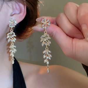 Gros plan sur de longues boucles d'oreilles feuilles d'or et zircons blancs
