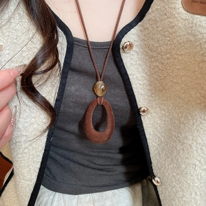Close-up of a vintage dark brown flocked resin oval pendant necklace on a beige sweater