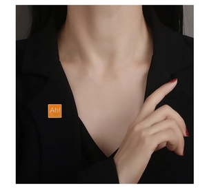 Détail d'un pin's orange en émail avec Ah! The Element of Surprise sur un blazer noir