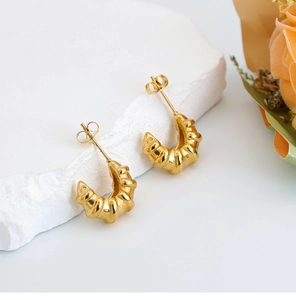Close-up of golden U-shaped twisted hoop earrings on white stone with dry flowers
