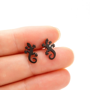 Détail d'un petit clou d'oreille gecko noir mat tenu entre les doigts pour taille réelle