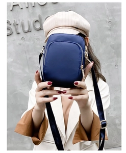 Detail of dark blue nylon mini crossbody bag with multiple zippers held by a model