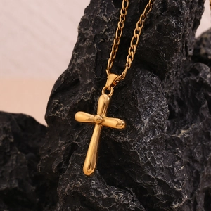 Detailed view of polished 18K gold plated cross pendant on a Figaro chain against rock