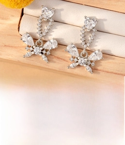 Detail of silver heart and butterfly zircon earrings on a wooden jewelry box background