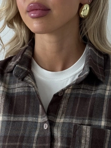 Golden organic bean shaped earrings paired with a vintage plaid shirt on a model