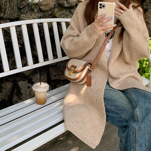 Dettaglio di cardigan beige e borsa a tracolla in tela e pelle con chiusura metallica