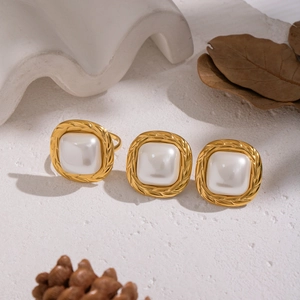 Vintage golden square pearl earrings with textured rope edge on marble stone surface