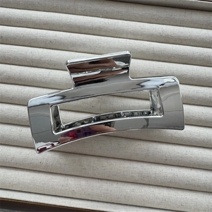 Detailed view of large silver metal hair claw clip with mirror finish on beige fabric