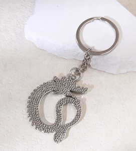 Close-up of a silver vintage dragon seahorse keychain on white stone texture surface