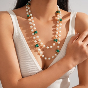 Detail of layered pearl necklace with square emerald-style gems on white ribbed top