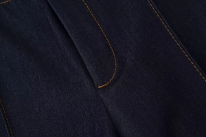 Détail du tissu denim bleu foncé avec des coutures orange contrastées et texture sergé