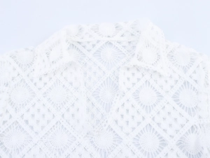 Detail of white hollow crochet top featuring a polo collar and intricate knit patterns
