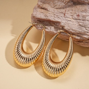Detail of gold oval hoop earrings with ribbed texture on natural stone surface