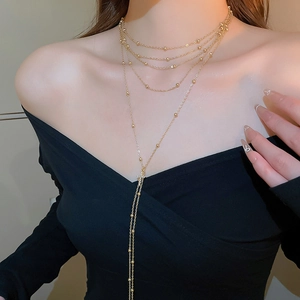 Close-up of a layered gold necklace with bead chain and Y-shape drop on a model