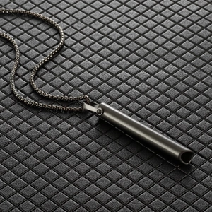 Detailed close-up of dark grey cylindrical meditation whistle pendant on box chain