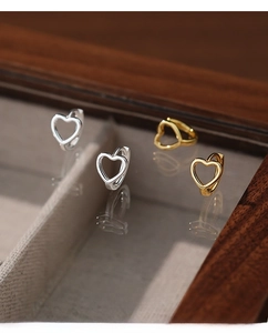 Detailed view of hollow heart hoop earrings in S925 silver and gold on a mirror surface