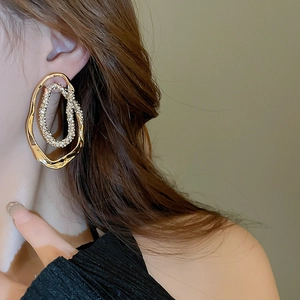 Detailed view of irregular gold oval earring with white crystals on female model