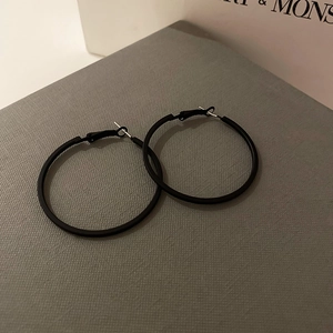 Close-up of minimalist black matte hoop earrings on a textured jewelry gift box