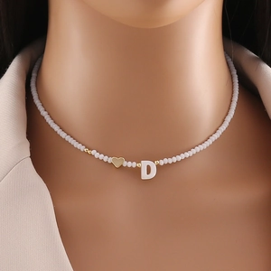 Close-up of shell letter D and heart pendant on white beaded necklace for women